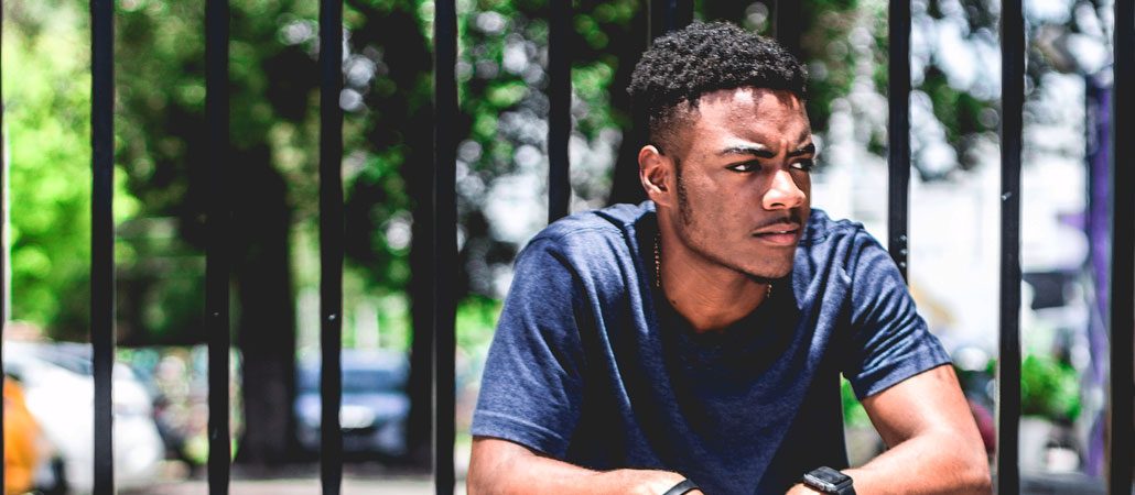 Young man sitting, fence in background