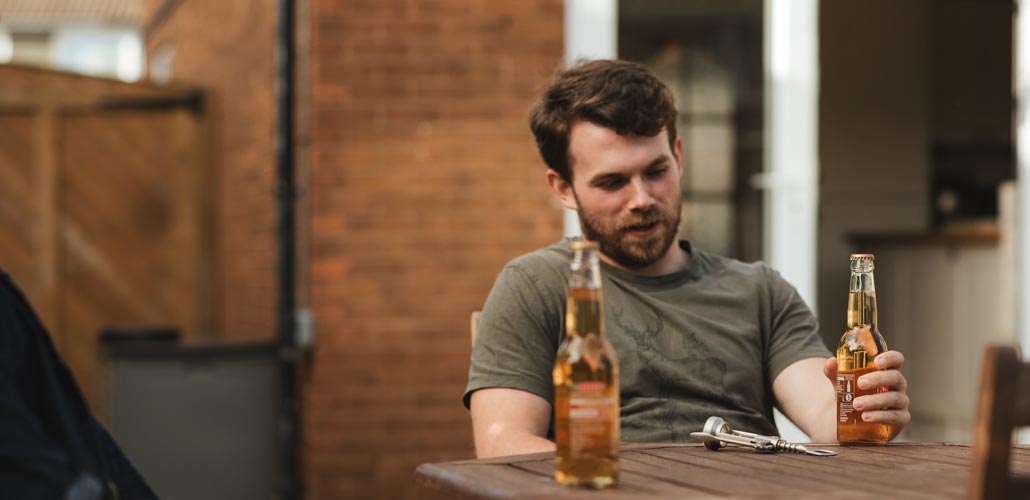 Man seated drinking a beer with a friend