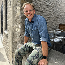 A picture of Justin Boudreau sitting on a ledge next to a stone building