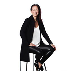 A professional photo of Adele Fox sitting on a stool in front of a transparent background