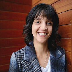 A photo of Maria Malouf smiling in front of a wooden wall