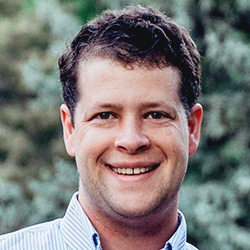 A headshot of Dr. Bradford Stucki smiling with some foliage in the background