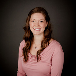 A photo of Caroline Crilley smiling in front of a plain dark background