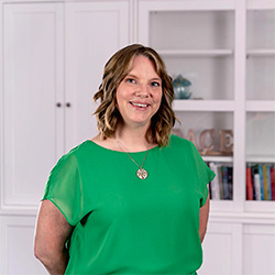 A photo of Dr. Kelly Penner Hutton smiling in front of a bookshelf