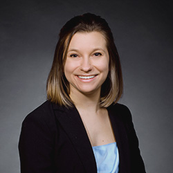 A professional headshot of Jenny Stevens smiling in front of a plain grey background