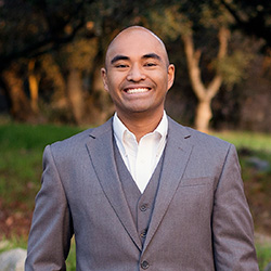 A photo of Chris Rabanera in a three-piece suit, smiling outside