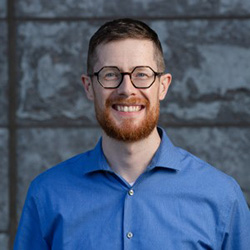 A photo of Rod Mitchell smiling in front of a stone wall